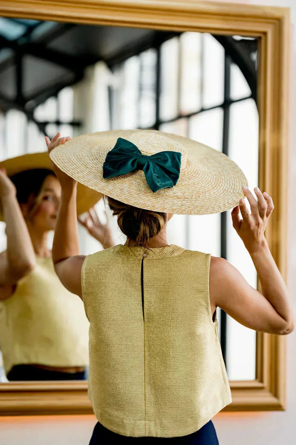 Image d'une dame se regardant dans un mirroir et portant une capeline Scarlett avec un noeud de couleur verte