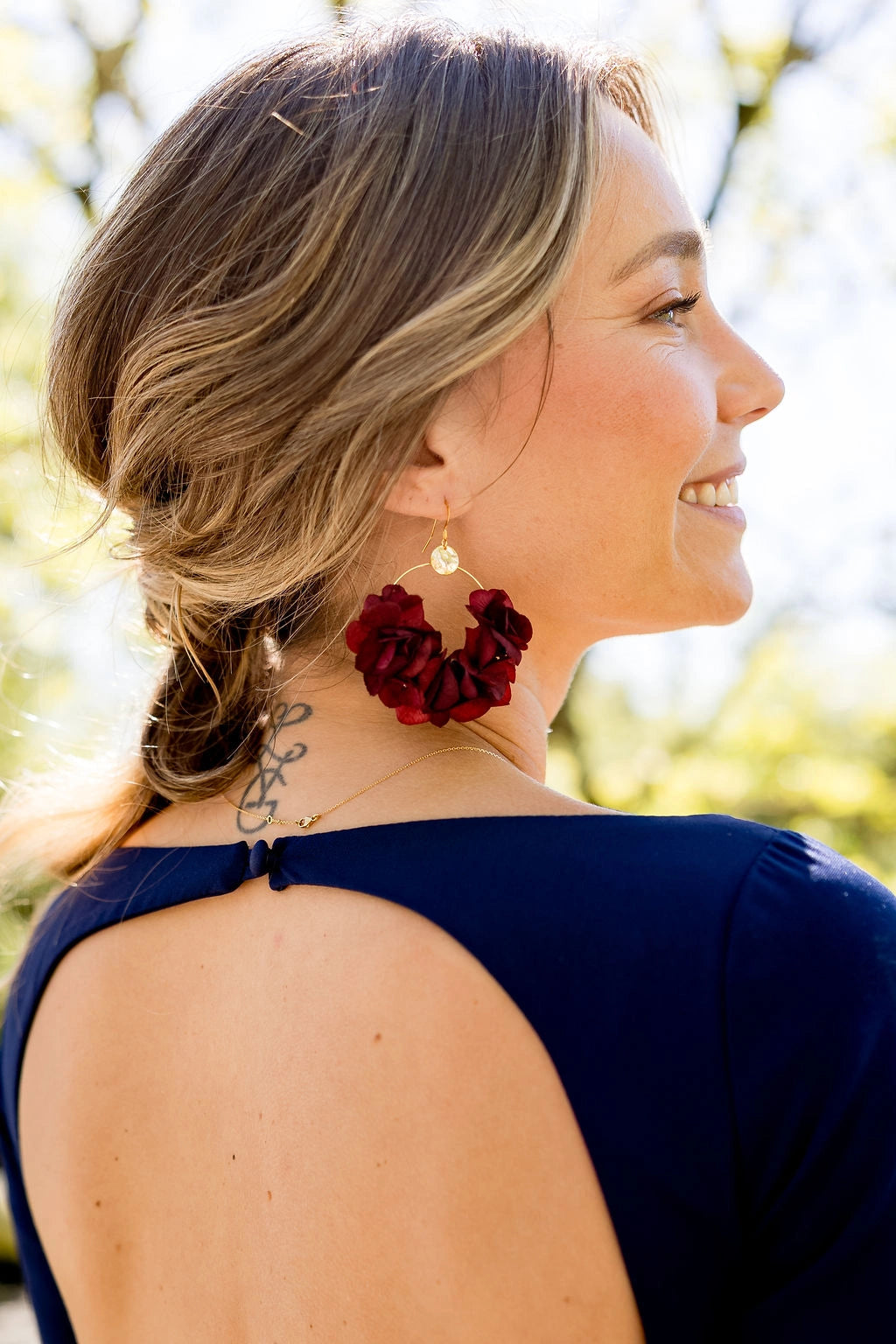 Jeune femme portant des boucles d'oreilles en forme de créoles avec des fleurs d'hortensia stabilisés de couleur bordeaux. Créé par Bellemond.