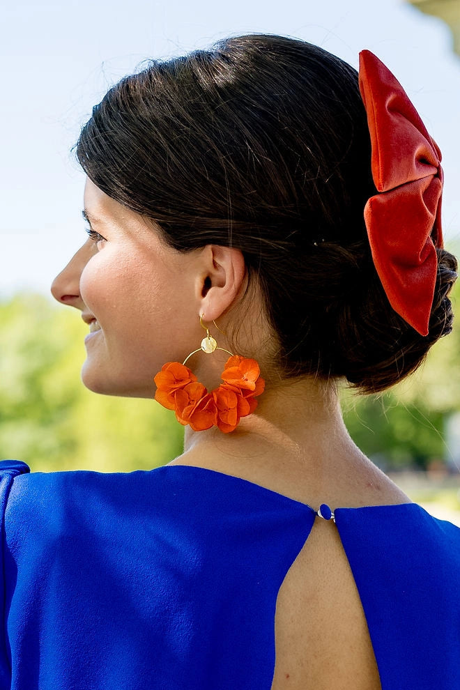 Jeune femme portant des boucles d'oreilles en forme de créoles composé de fleurs d'hortensia stabilisés de couleur orange. Créé par Bellemond.