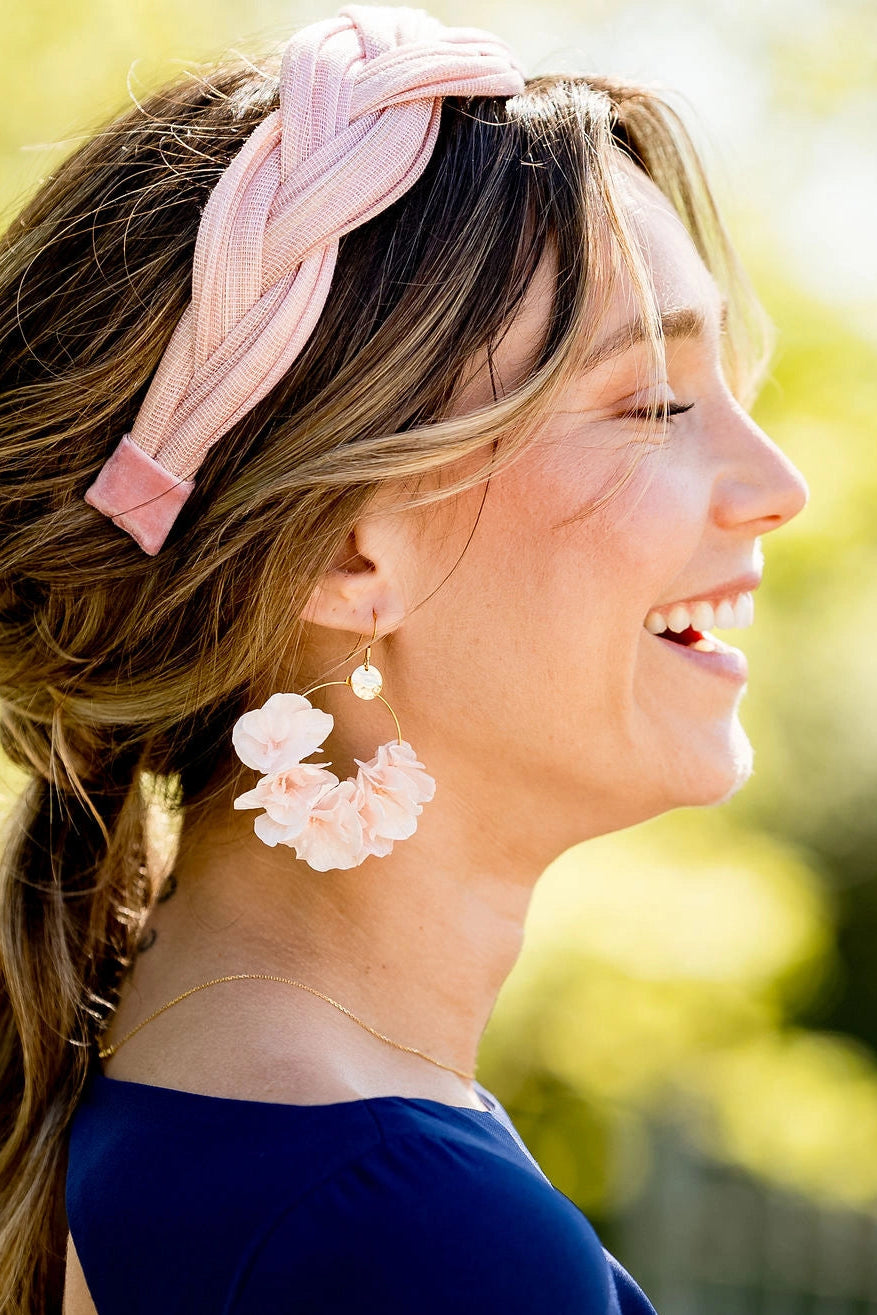 Jeune femme portant des boucles d'oreilles de couleur rose pâle montées sur créoles et fabriqué en hortensia stabilisé. Créé par Bellemond.