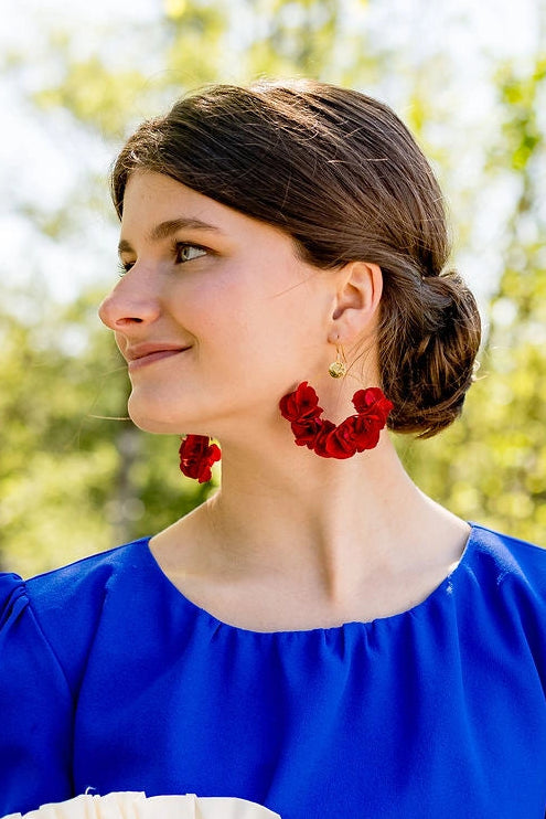 Jeune femme en robe bleue roi portant aux oreilles des boucles d'oreilles en fleurs d'hortensia stabilisées de couleur rouge montés sur créoles. Créé par Bellemond.