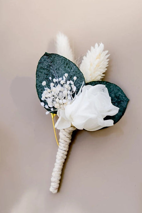 Boutonnière dans les tons blancs et verts avec une mini rose, mini gypsophile, phalaris, eucalyptus et lagurus stabilisé ou séché. Créé par Bellemond.