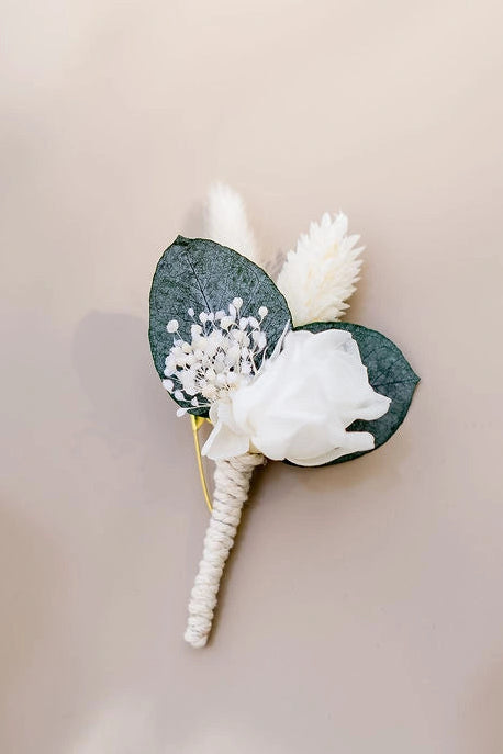 Boutonnière composée de fleurs séchées et stabilisées dans les tons verts et blancs. Créé par Bellemond.