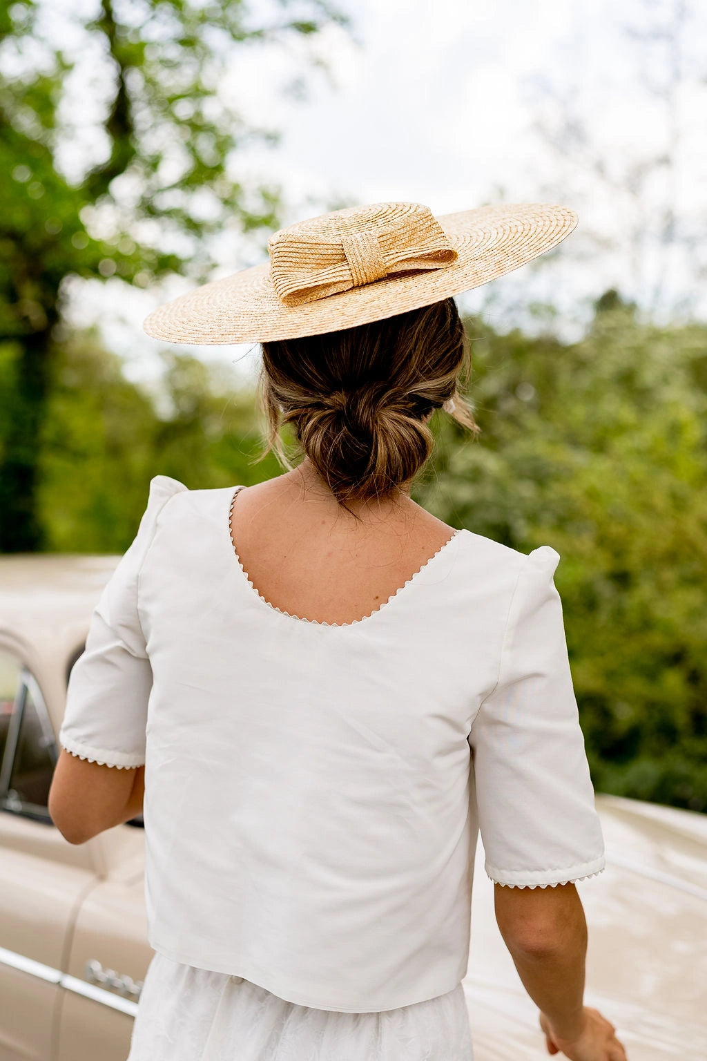 Jeune mariée de dos portant sur la tête une capeline en paille naturelle surmonté d'un noeud en paille naturelle sur l'arrière du chapeau. Créé par Bellemond.