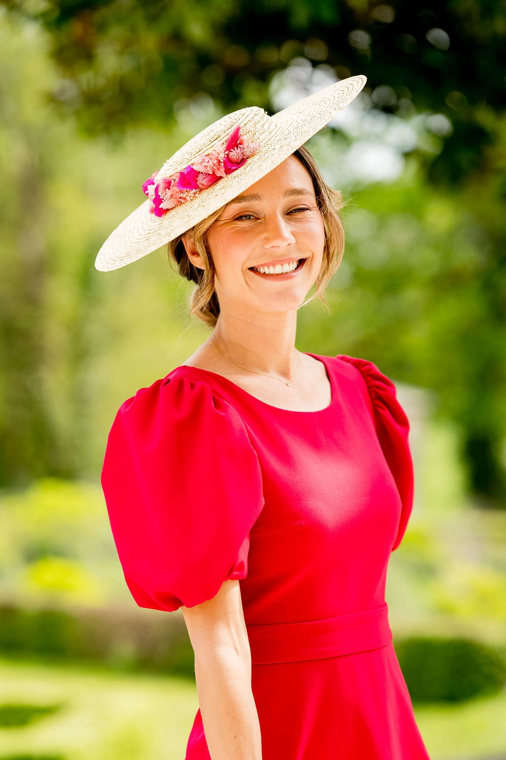 Jeune femme habillée d'une robe rouge portant une capeline avec des fleurs séchées et stabilisées de couleur rose, fuchsia et corail. Créé par Bellemond.