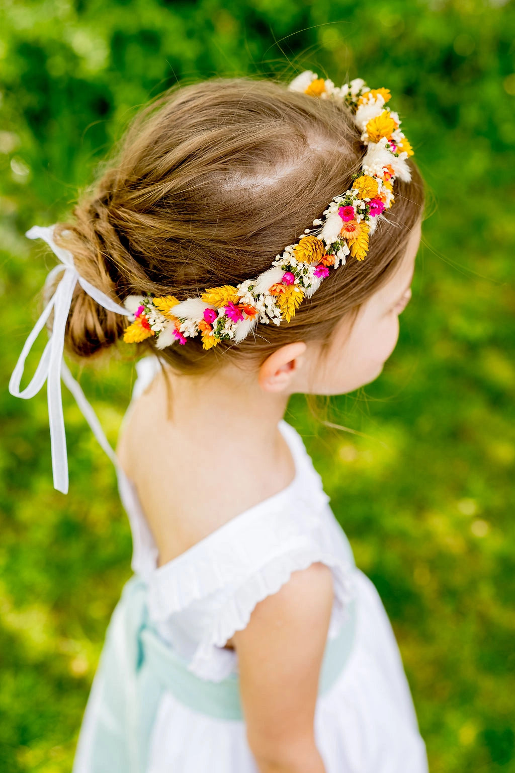 Petite fille avec une robe blanche portant une couronne de fleurs séchées multicolore sur la tête. Créé par Bellemond.