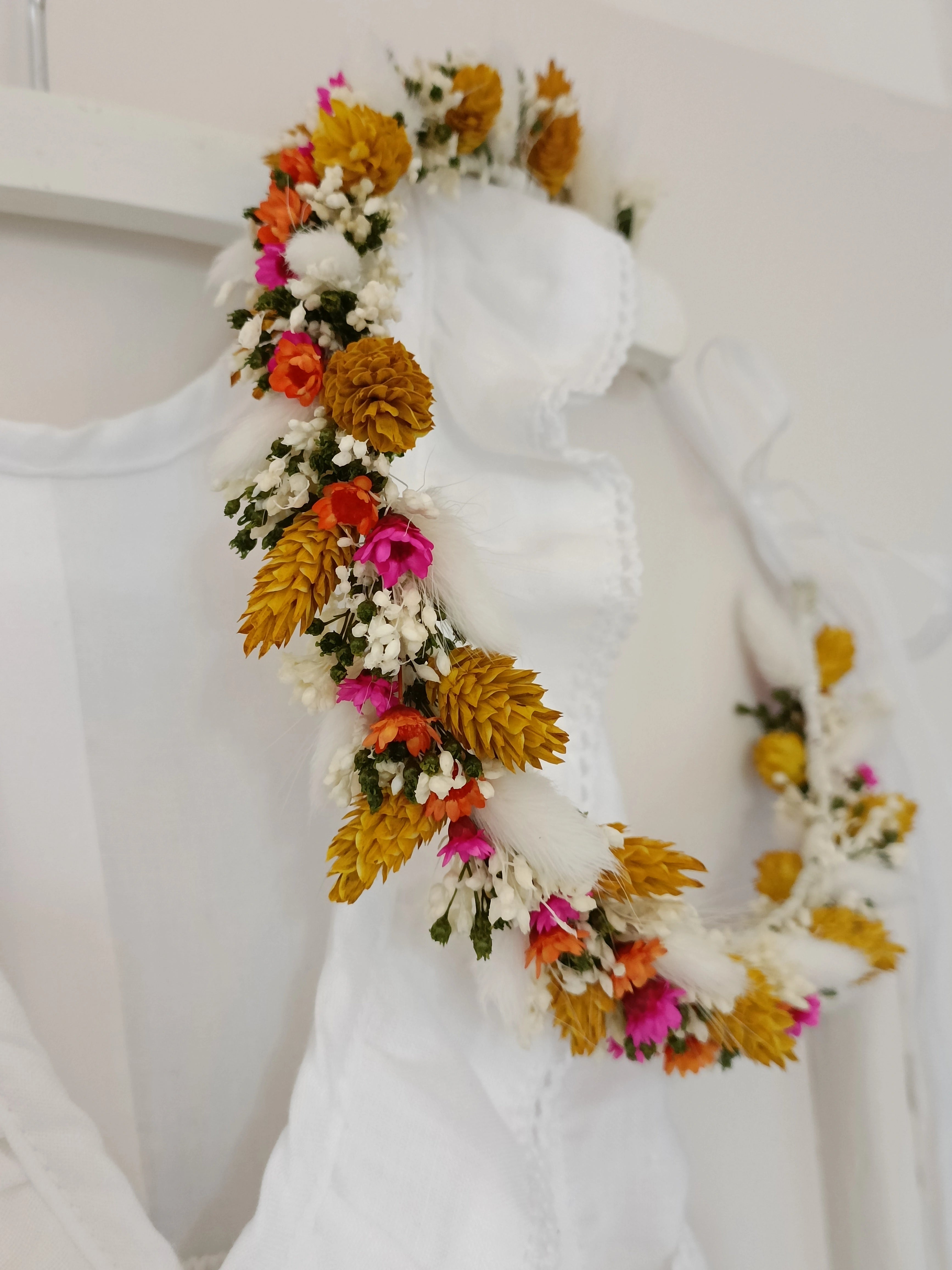 Couronne de fleurs séchées et stabilisées accrochée sur un ceintre avec une petite robe blanche. Créé par Bellemond.