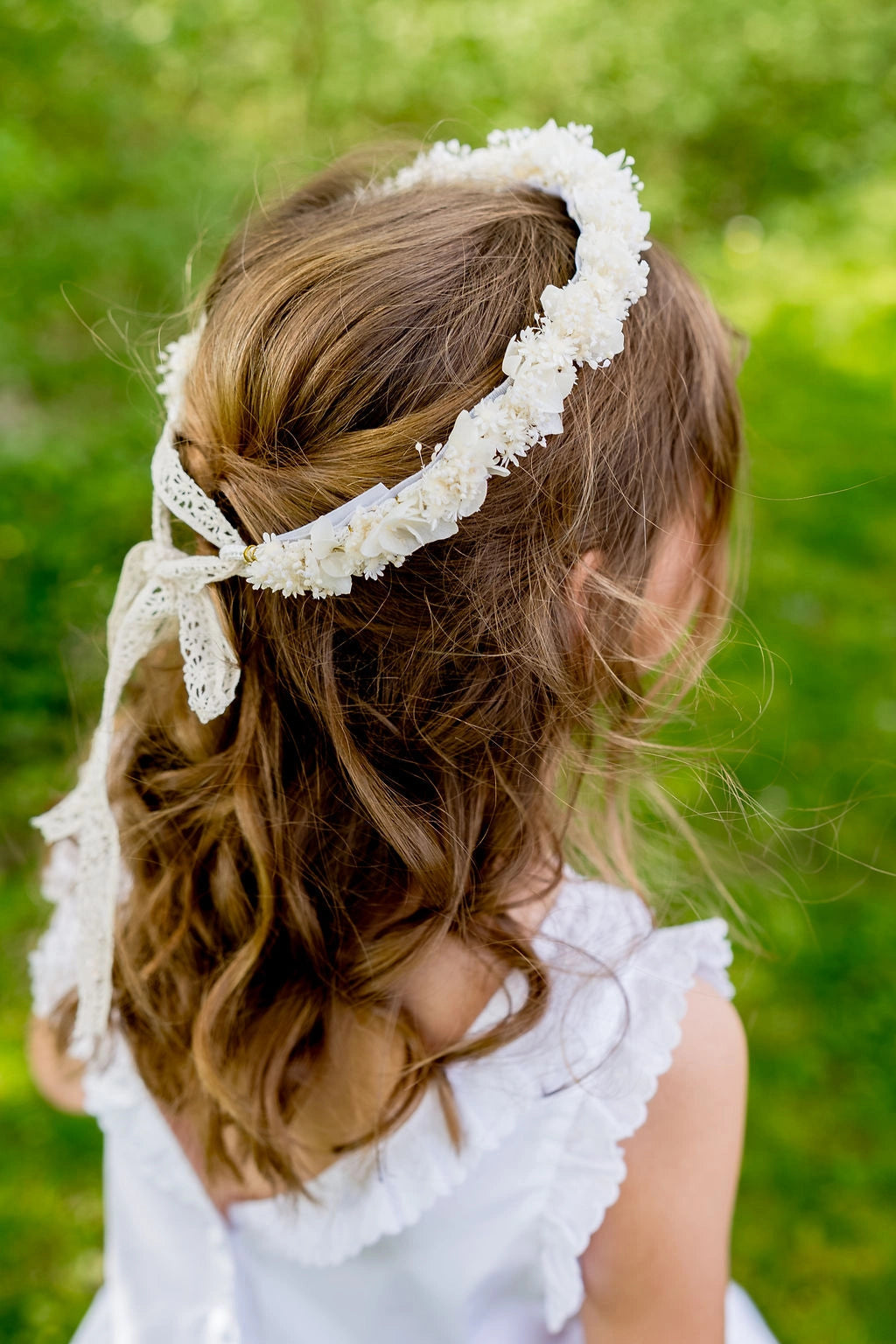 Fille habillée de blanc se tenant de dos avec dans les cheveux une couronne de fleurs séchées et stabilisées de couleur blanc. Créé par Bellemond.