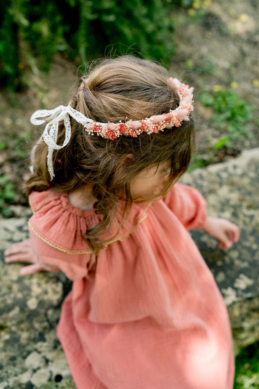 Petite fille habillée d'une robe couleur tomette avec une couronne de fleurs séchées sur la tête dans les tons roses. Créé par Bellemond.
