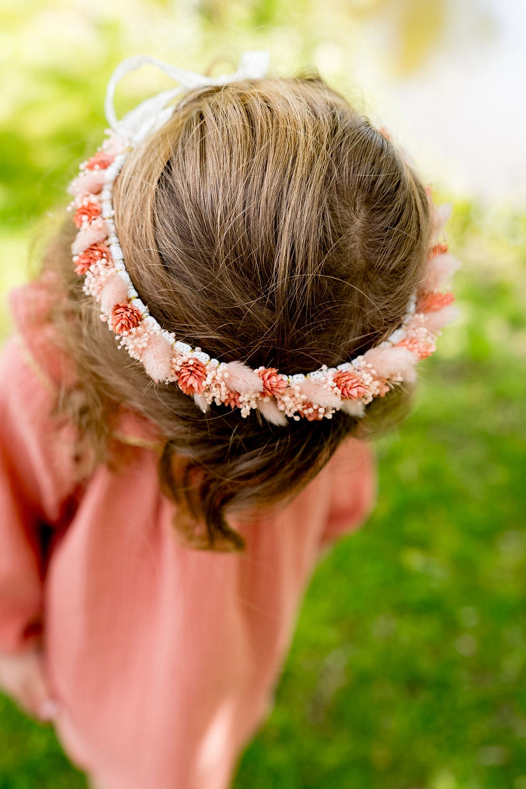 Petite fille montrant le haut de sa tête sur laquelle est posée une couronne fleurie en fleurs séchées et stabilisées de couleur roses. Créé par Bellemond.