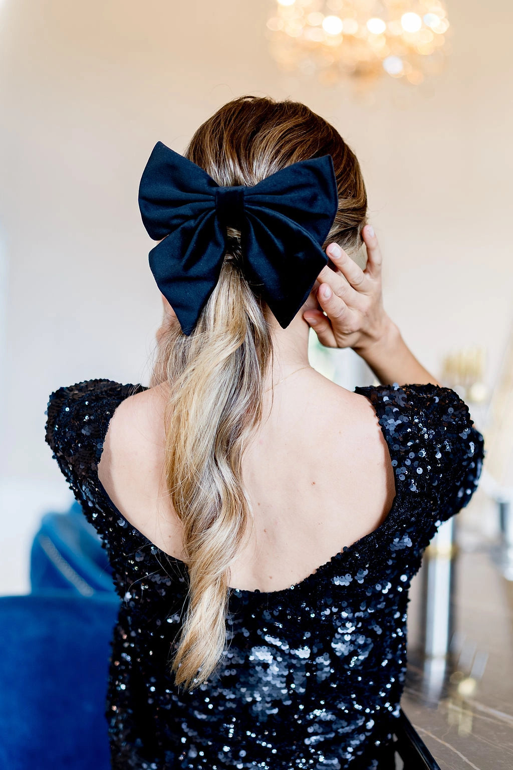 Jeune femme se tenant de dos avec un top noir à sequins ayant dans les cheveux un noeud en velours noir monté sur barrette. Créé par Bellemond.