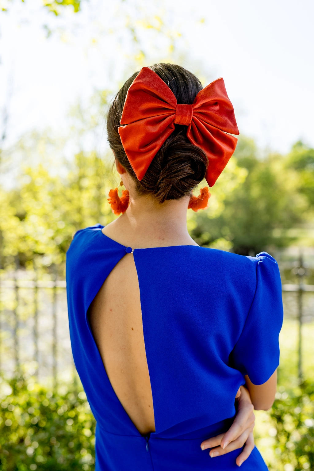 Jeune femme de dos dans une robe bleue roi avec dans les cheveux un noeud en velours orange monté sur barrette. Créé par Bellemond.