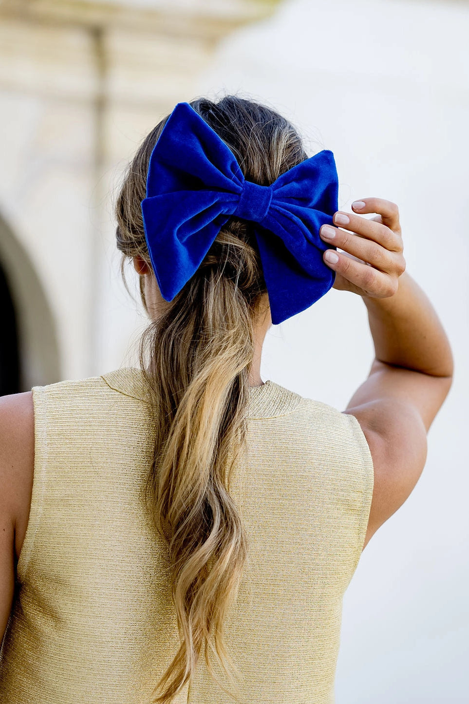 Jeune femme se tenant de dos avec dans les cheveux un noeud en velours bleu roi de type barrette. Créé par Bellemond.