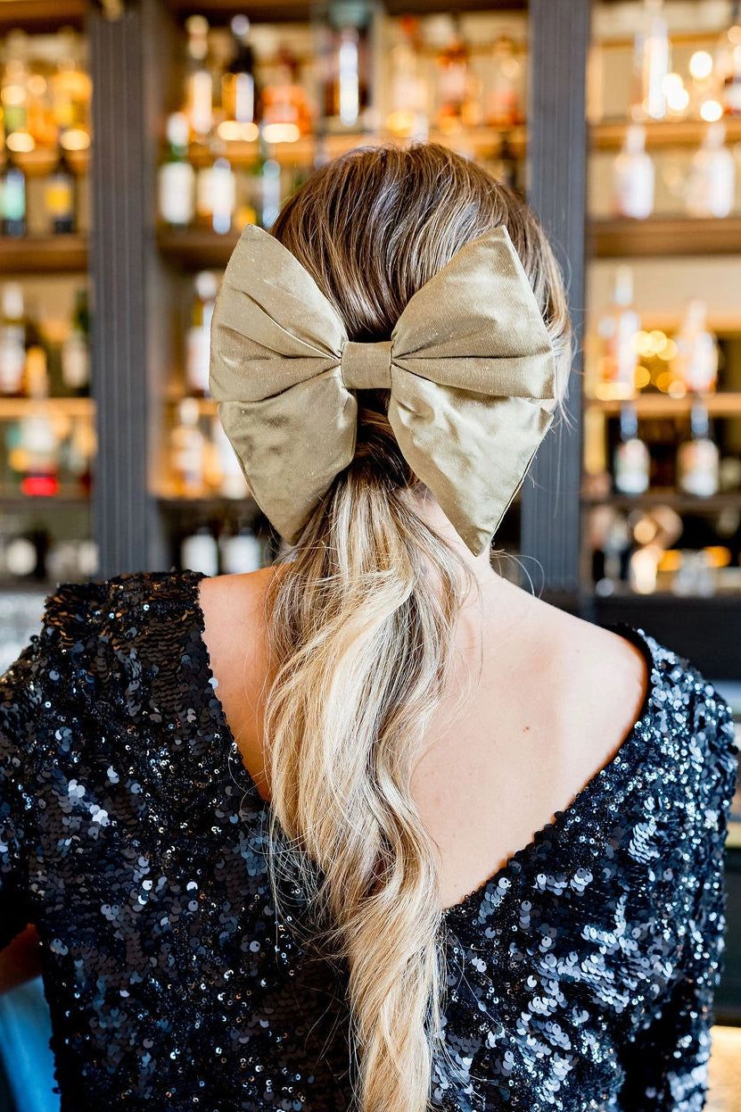Jeune femme en haut noir à sequins avec dans ses cheveux une barrette avec un noeud en soie doré. Créé par Bellemond.