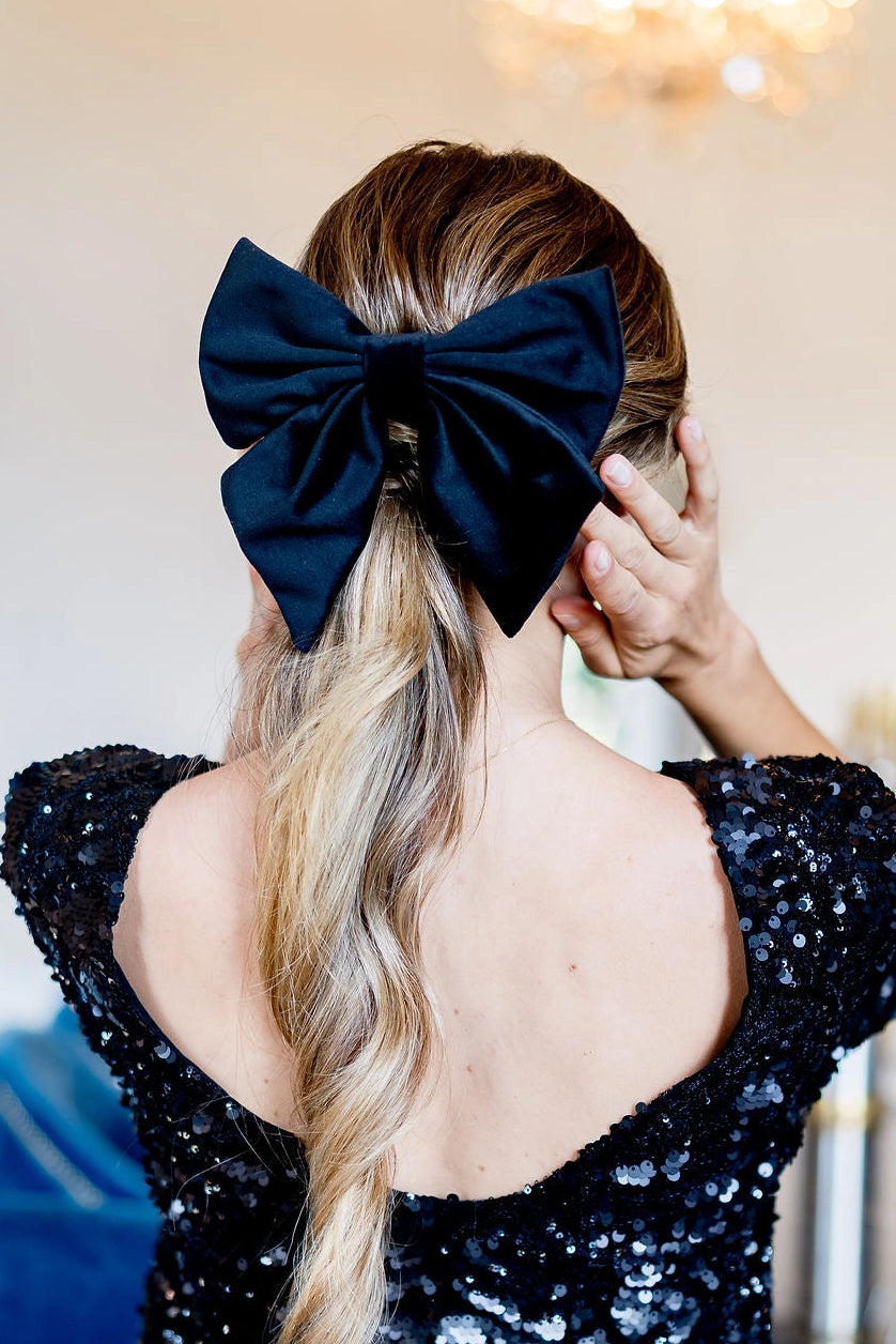 Jeune femme de dos portant un haut en sequins noirs et ayant dans les cheveux un noeud en velours noir comme une barrette. Créé par Bellemond.