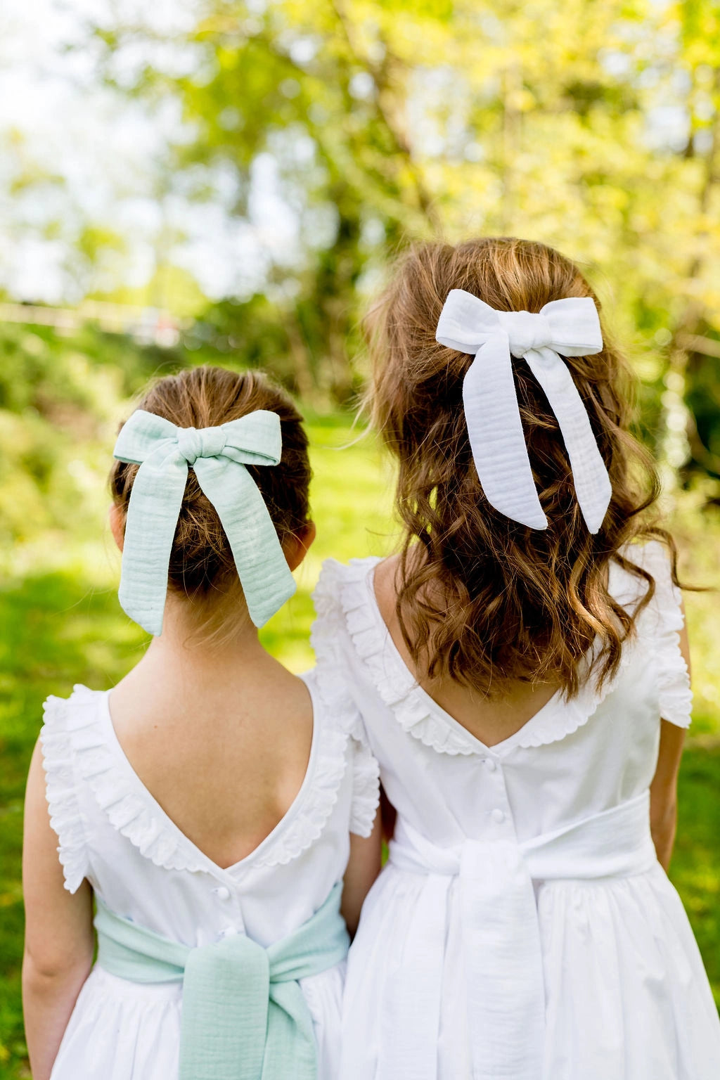 Deux petites filles de dos avec dans les cheveux des barrettes avec un noeud blanc et vert menthe. Créé par Bellemond.