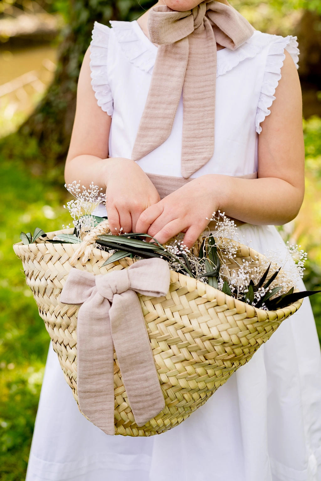 Petite fille de cortège qui tient un petit panier à la main sur lequel se trouve un noeud de couleur sable. Créé par Bellemond.