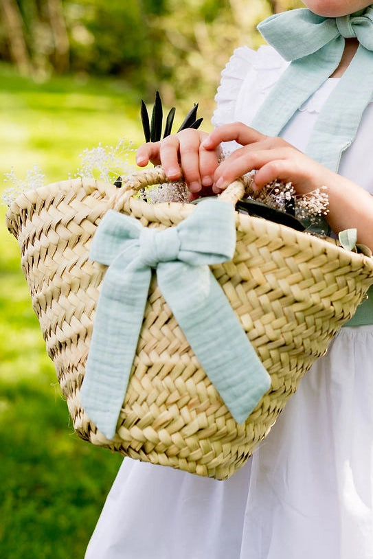 Petit panier en doum porté par une petite fille d'un cortège de mariage avec un noeud de couleur vert menthe. Créé par Bellemond.