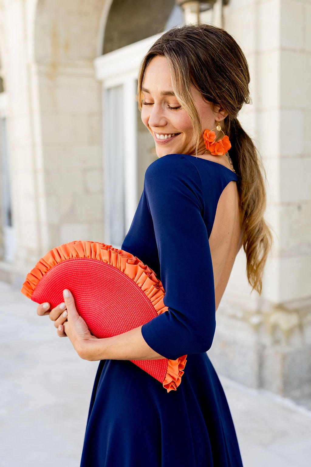 Jeune femme habillée de bleu marine portant à la main une pochette en demie lune froncée de couleur rouge. Créé par Bellemond.