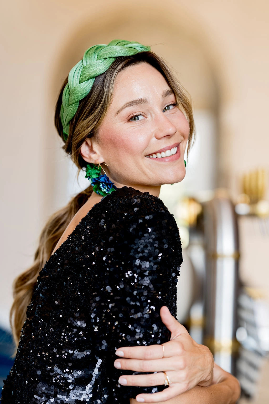 Jeune femme habillée d'un haut noir à paillettes et portant un serre-tête en sinamay vert tressé. Créé par Bellemond.