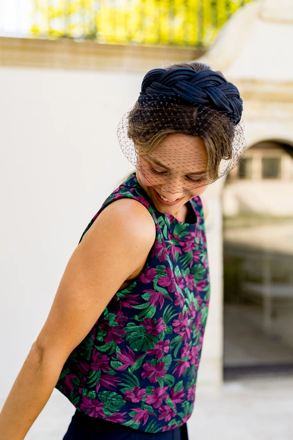 Jeune femme portant un top multicolore et ayant sur la tête un serre-tête en sinamay tressé de couleur bleue marine avec une voilette tombant sur le devant du visage. Créé par Bellemond.