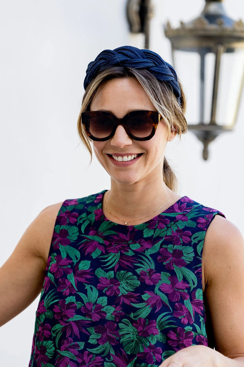 Jeune femme avec un top multicolore et portant des lunettes de soleil, ayant dans les cheveux un serre-tête tressé en sinamay de couleur bleue marine. Créé par Bellemond.