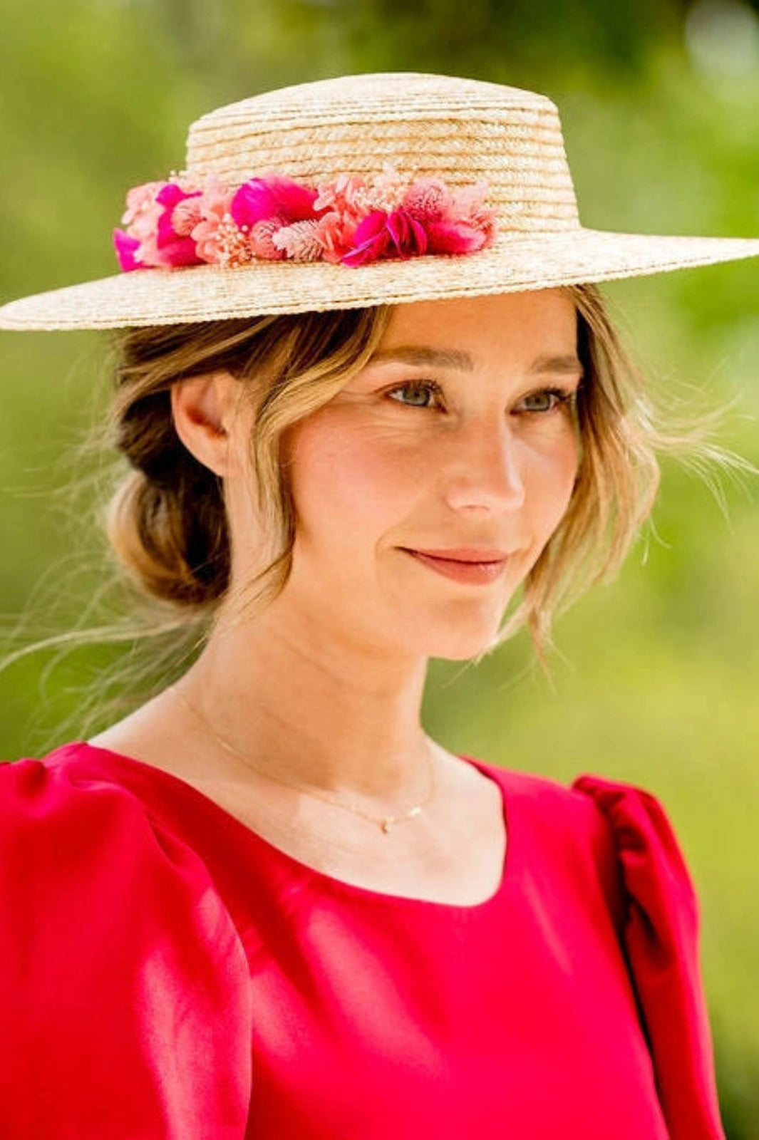 Jeune femme portant sur la tête un canotier en paille naturelle surmontée de fleurs séchées et stabilisées dans les tons roses, fuchsia et corail. Créé par Bellemond.