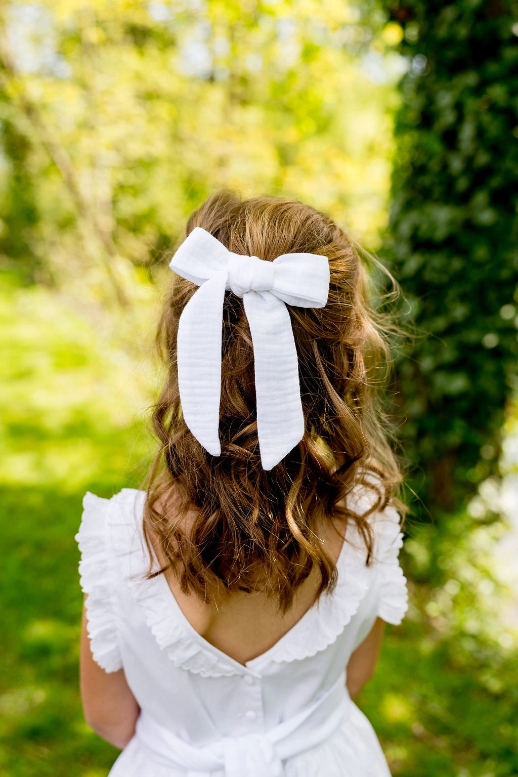 Petite fille avec cheveux lachés de dos portant dans les cheveux une barrette avec un noeud blanc en tissu. Créé par Bellemond.