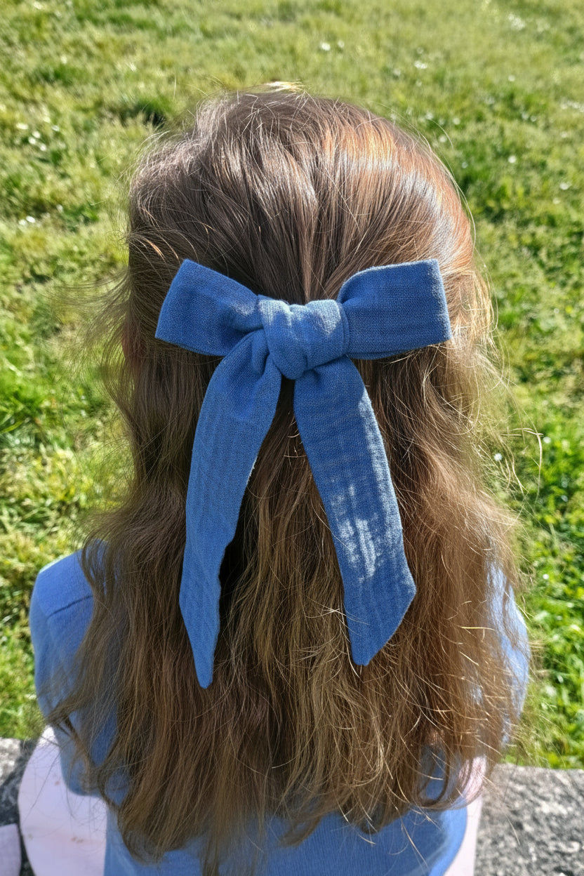 Petite fille avec cheveux lâchés ayant dans les cheveux une noeud sous forme de barrette en gaze de coton bleu-gris. Créé par Bellemond.