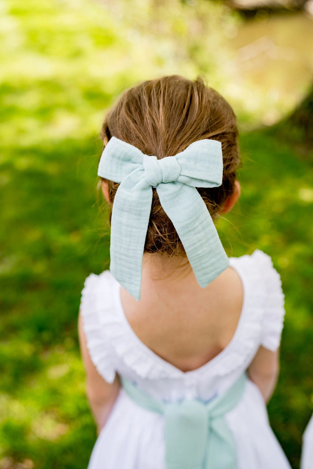 Petite fille de dos avec cheveux attachés avec une barrette à nœud, de couleur vert menthe.  Créé par Bellemond.