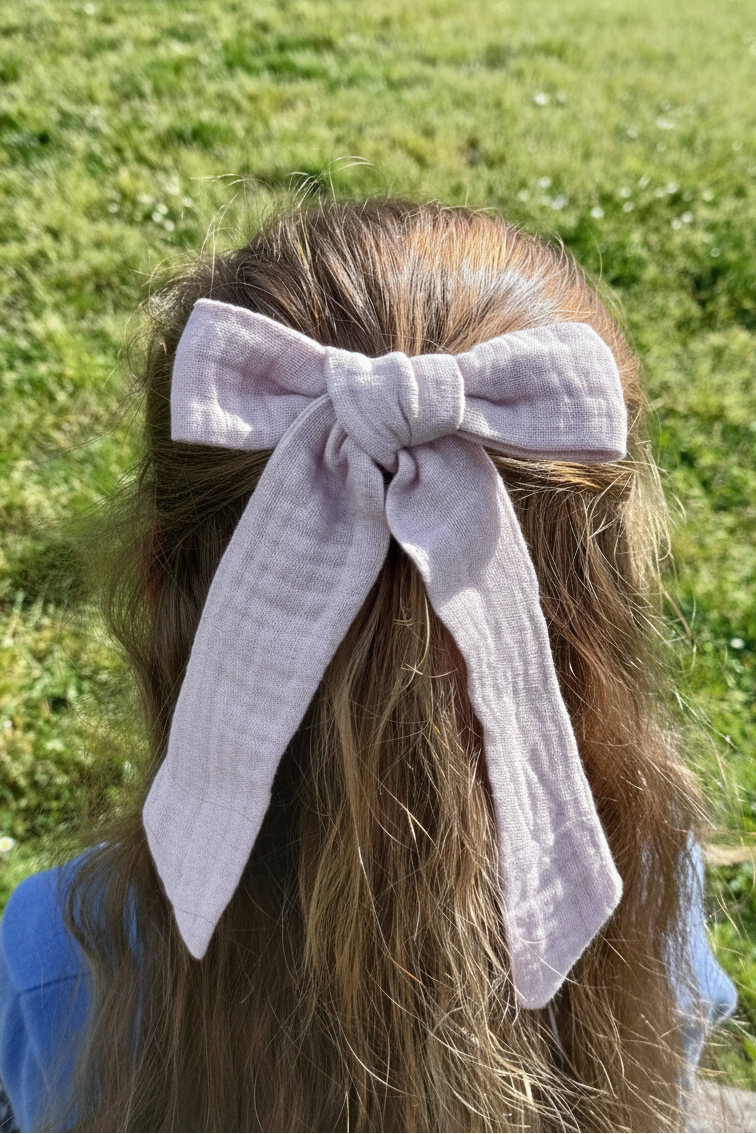 Petite fille de dos avec les cheveux lâchés dans lesquels se trouve une barrette en gaze de coton vieux rose. Créé par Bellemond.