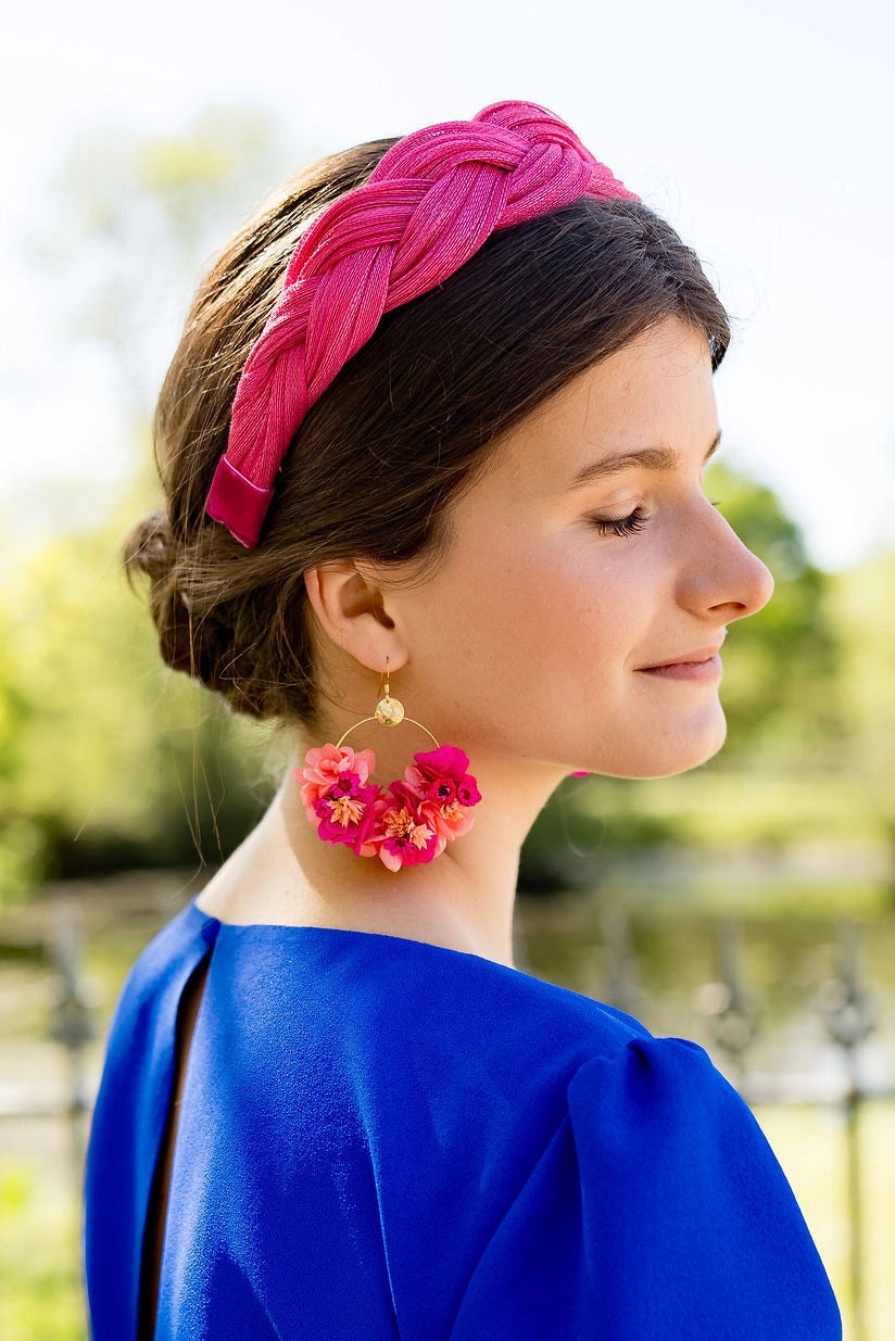 Jeune femme avec des boucles d'oreilles en forme de créoles avec des fleurs stabilisées et séchées de couleur fuchsia et corail. Créé par Bellemond.