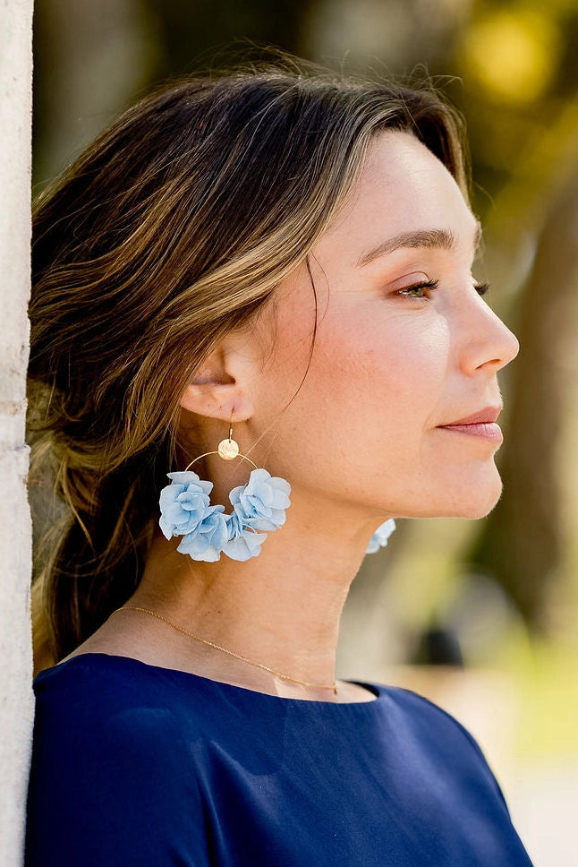 Jeune femme avec des boucles d'oreilles en hortensia stabilisé de couleur bleu clair, monté sur créoles dorées. Créé par Bellemond.