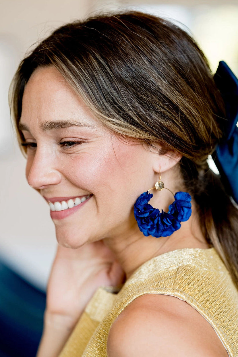 Jeune femme portant des boucles d'oreilles en forme de créoles surmontés de fleurs d'hortensia stabilisées de couleur bleu. Créé par Bellemond. 