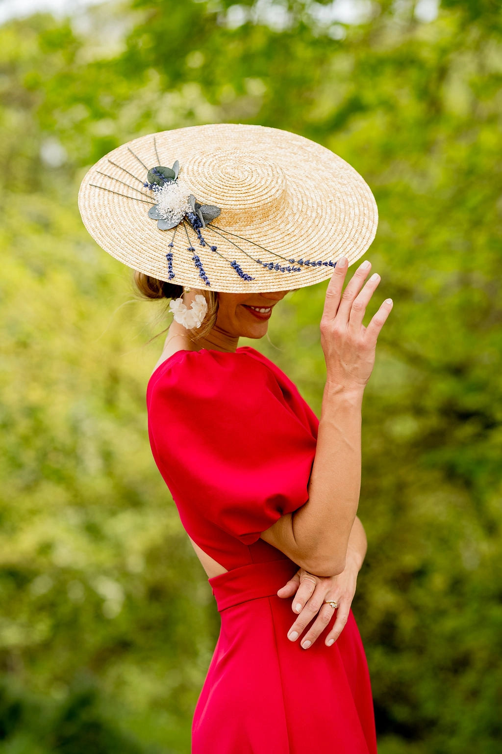 Jeune femme en robe rouge portant sur la tête une capeline en paille naturelle surmontée de lavande, de gypsophile et de feuilles d'eucalyptus. Créé par Bellemond. 