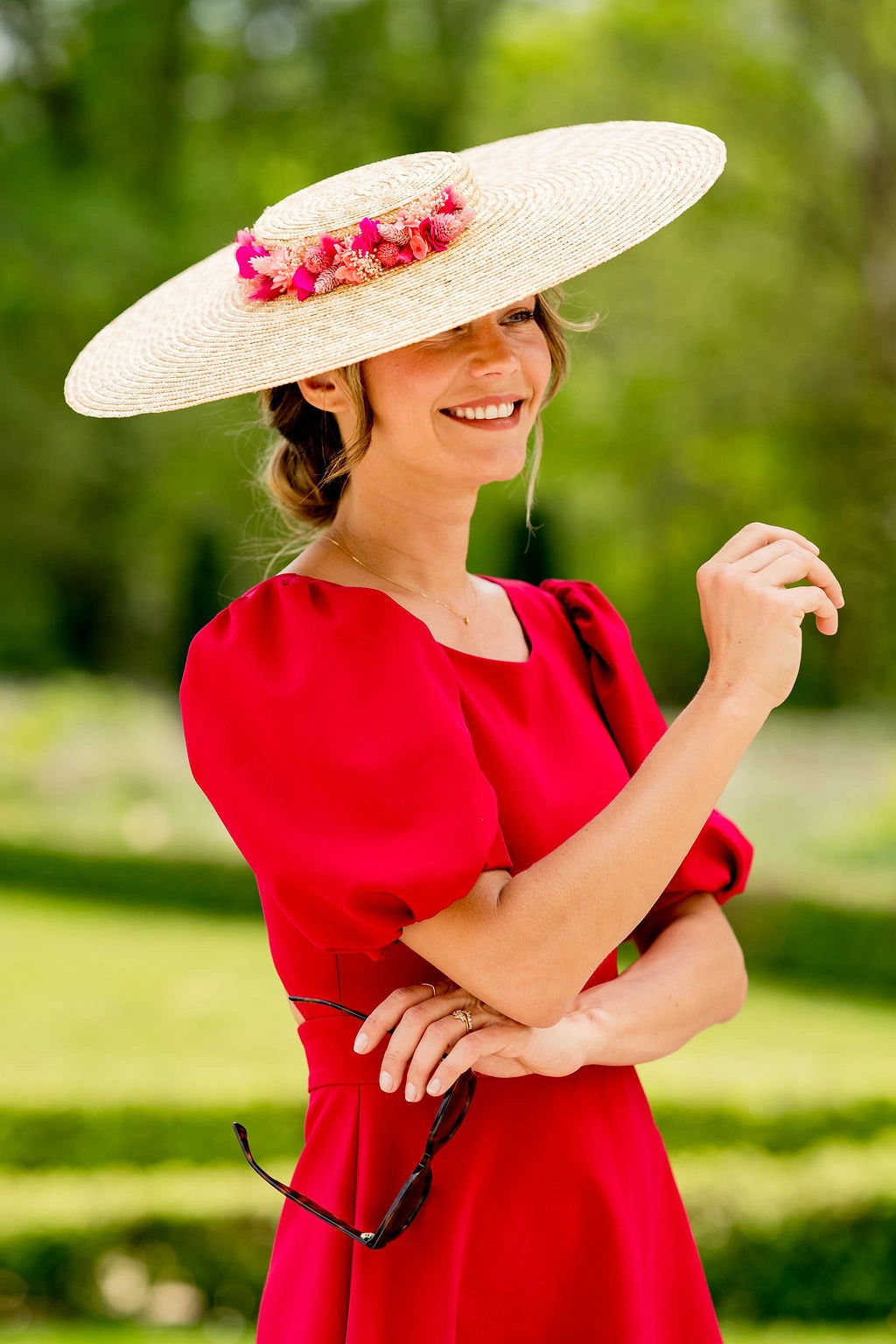 Jeune femme habillée de rouge portant sur la tête une capeline surmontée de fleurs séchées et stabilisées dans les ton roses, fuchsia et corail. Créé par Bellemond. 