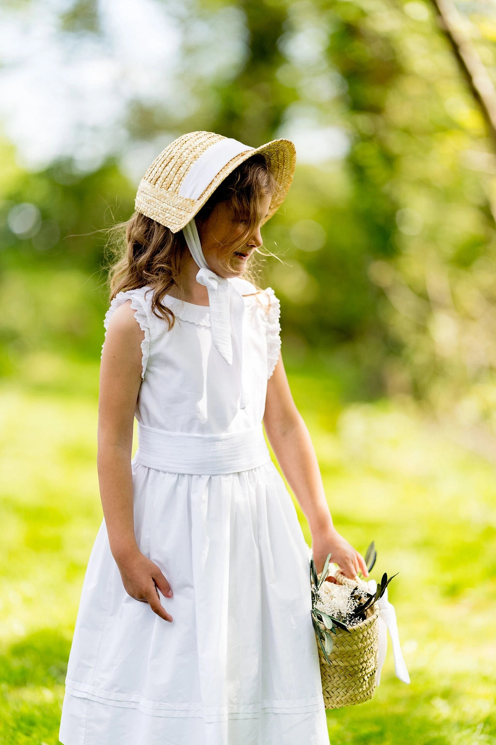 Petite fille habillée de blanc pour un cortège ou un baptême portant un petit panier et un chapeau en paille de type creusois. Un ruban blanc tient le chapeau avec un noeud sous le menton. Créé par Bellemond. 