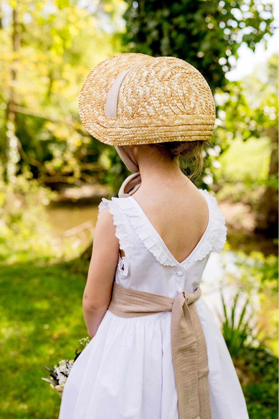 Petite fille de cortège portant un chapeau de paille de type calotte avec un ruban couleur sable en coton. Créé par Bellemond. 