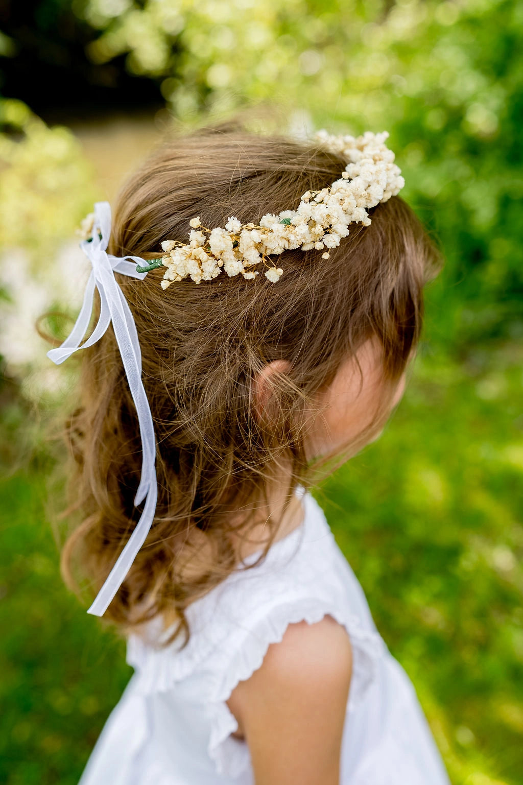 Petite fille de profil portant sur la tête une couronne de fleurs stabilisées composée de gypsophile naturel. Créé par Bellemond.