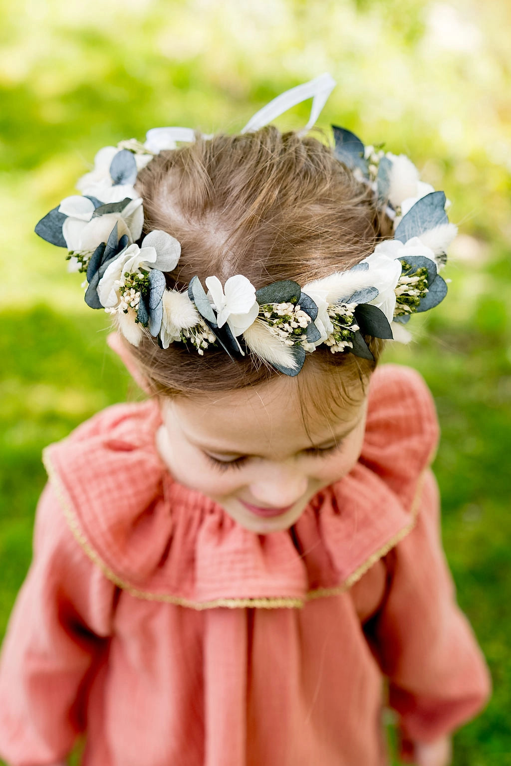 Petite fille portant une couronne de fleurs composée de fleurs séchées et stabilisées blanches et vertes : eucalyptus, hortensia et broom. Créé par Bellemond.