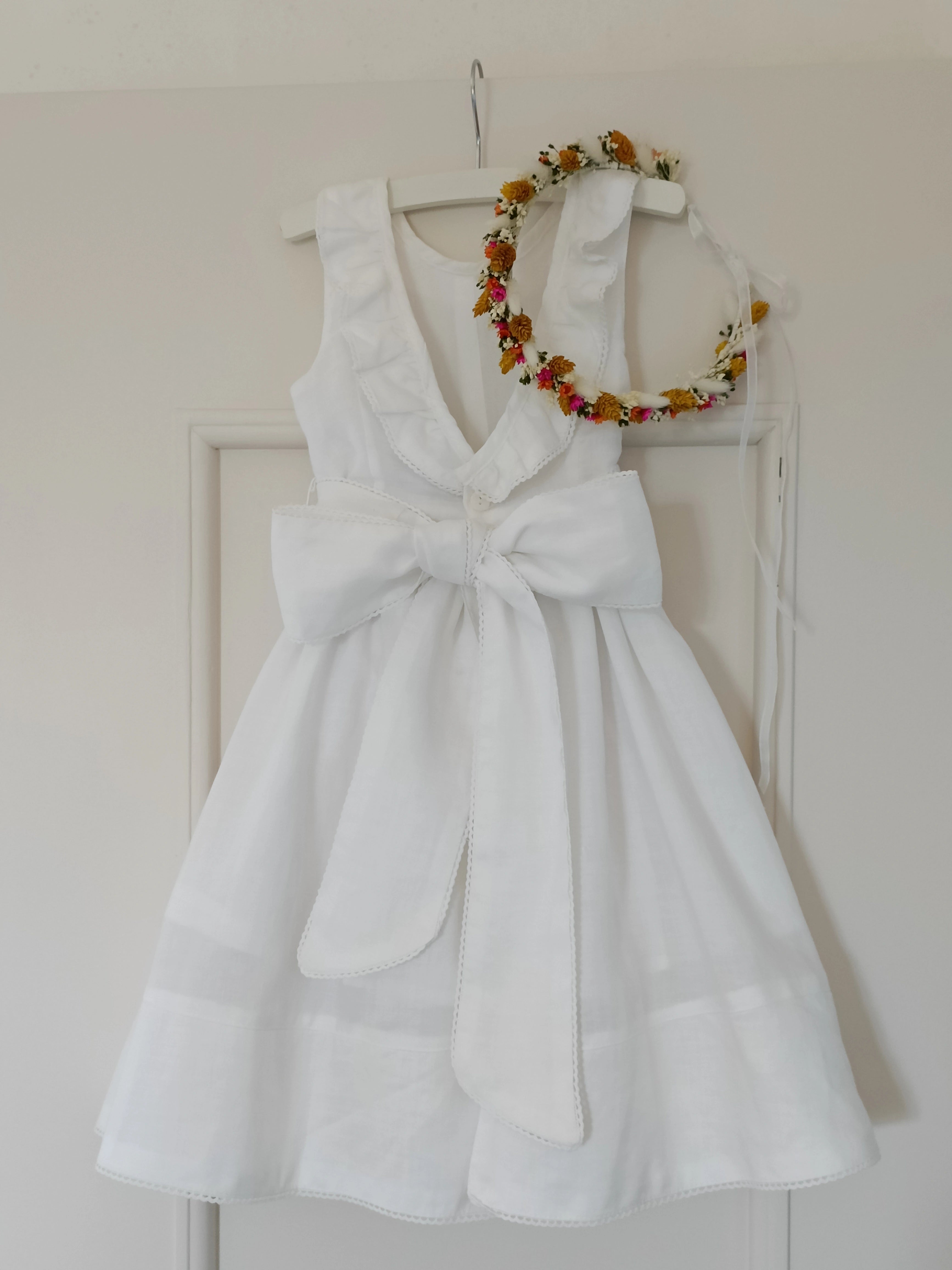 Petite robe d'enfant blanche suspendue avec une couronne de fleurs séchées multicolore. Créé par Bellemond. 