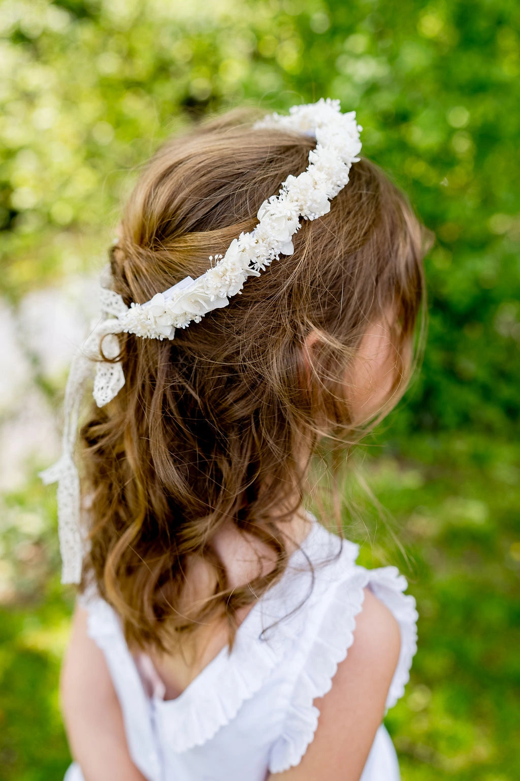 Petite fille de dos avec dans la coiffure une couronne composée de fleurs séchées et stabilisées blanches. Créé par Bellemond. 