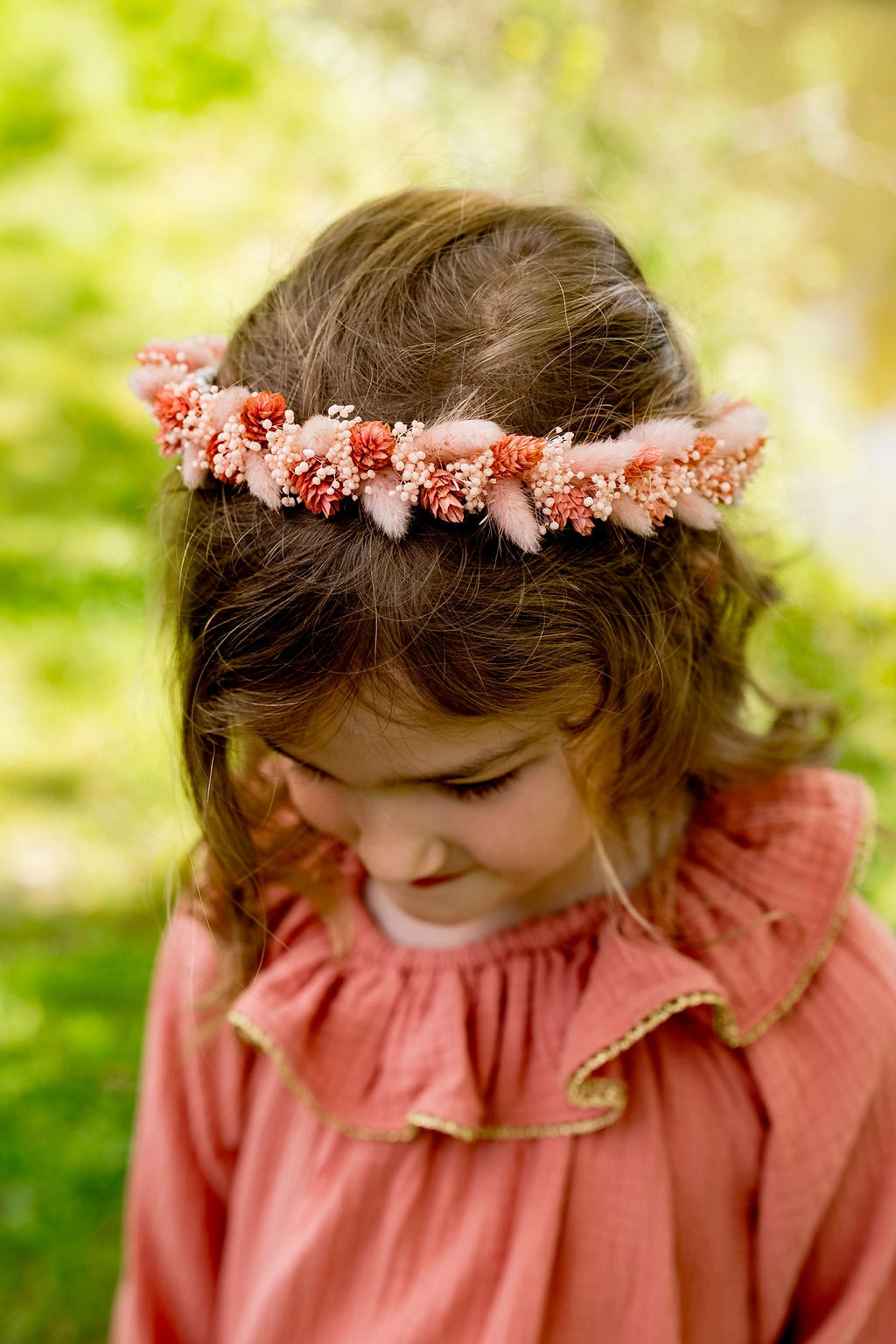 Petite fille habillée d'une robe couleur tomette portant sur la tête une couronne de fleurs séchées dans les tons roses. Créé par Bellemond. 
