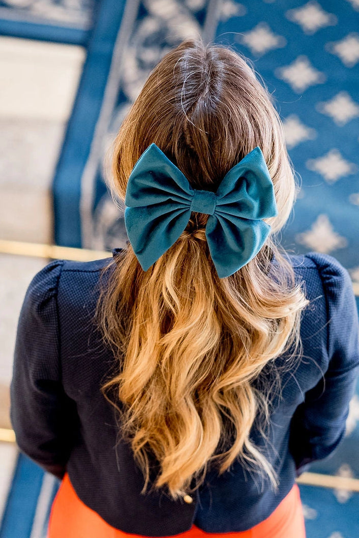 Jeune femme se tenant de dos avec un haut bleu ayant dans les cheveux un noeud sous forme de barrette en velours de couleur bleu. Créé par Bellemond. 