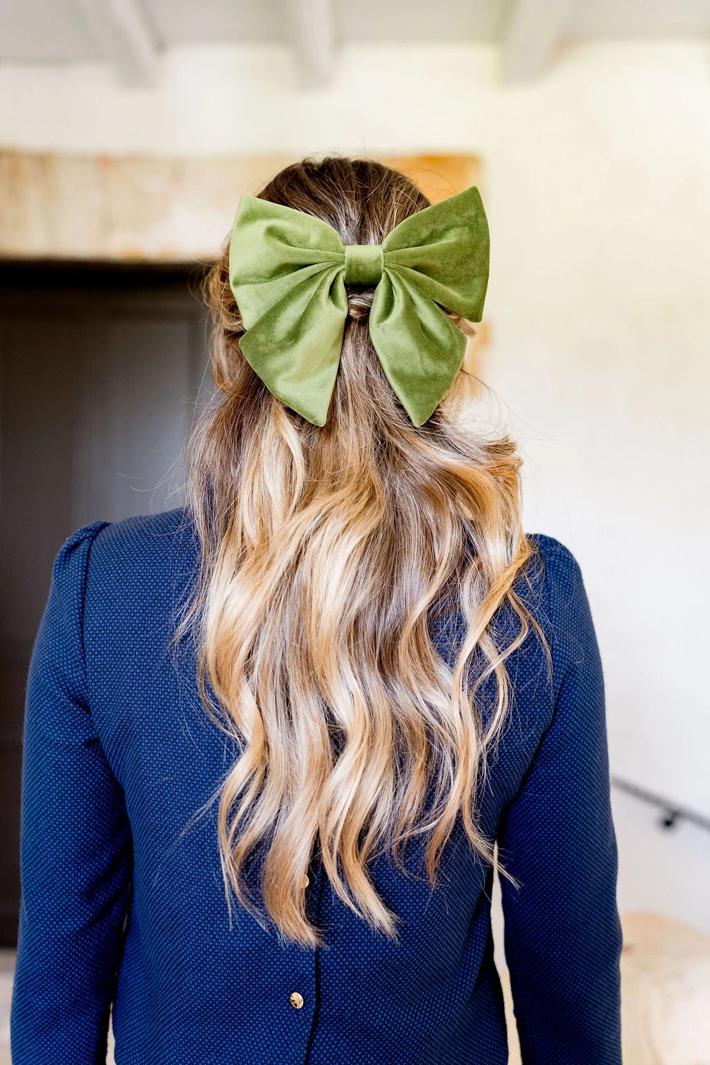 Jeune femme se tenant de dos avec un haut bleu. Elle a les cheveux lâchés et dans les cheveux il y a une barrette en velours vert olive monté sur barrette. Créé par Bellemond. 