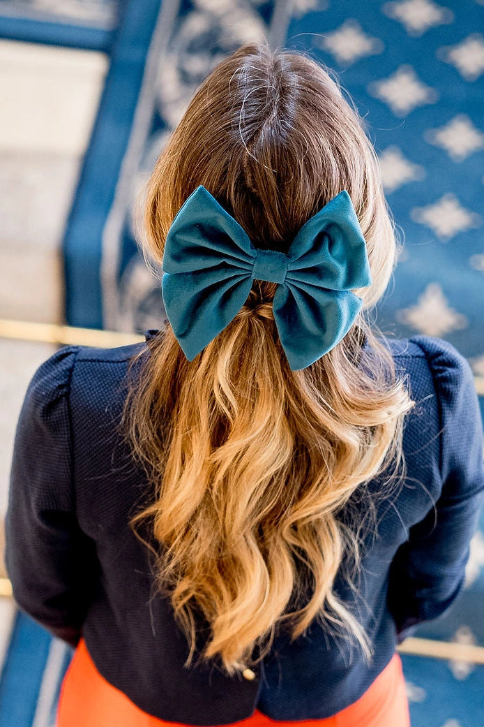 Jeune femme se tenant dans les escaliers avec dans les cheveux un noeud en velours bleu monté sur barrette. Créé par Bellemond. 