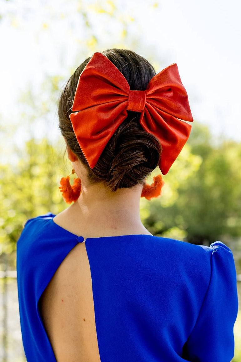 Jeune femme en robe bleue roi avec dans les cheveux un noeud en velours de type barrette de couleur orange. Créé par Bellemond. 