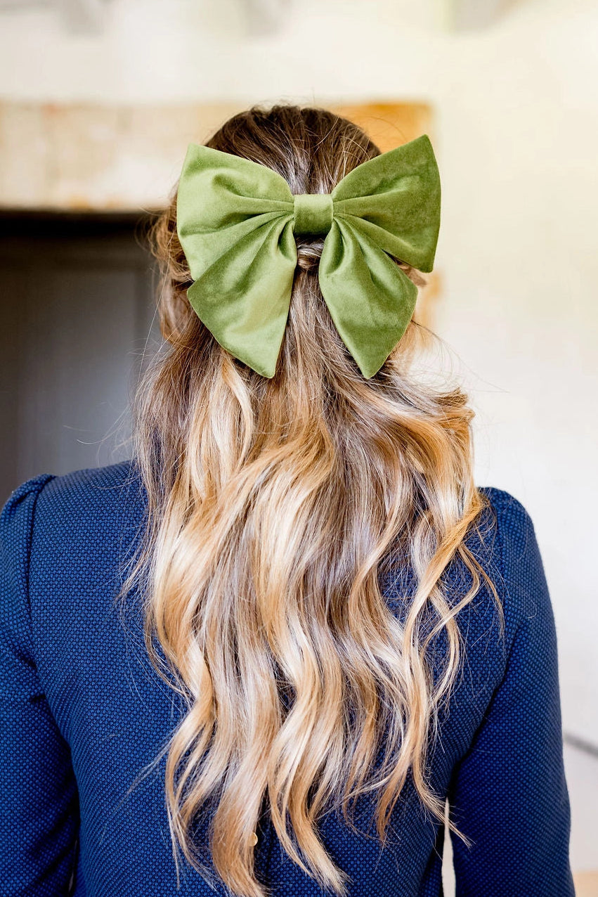Jeune femme se tenant de dos avec les cheveux lachés dans lesquels est attaché une barrette surmonté d'un noeud en velours de couleur vert olive. Créé par Bellemond. 