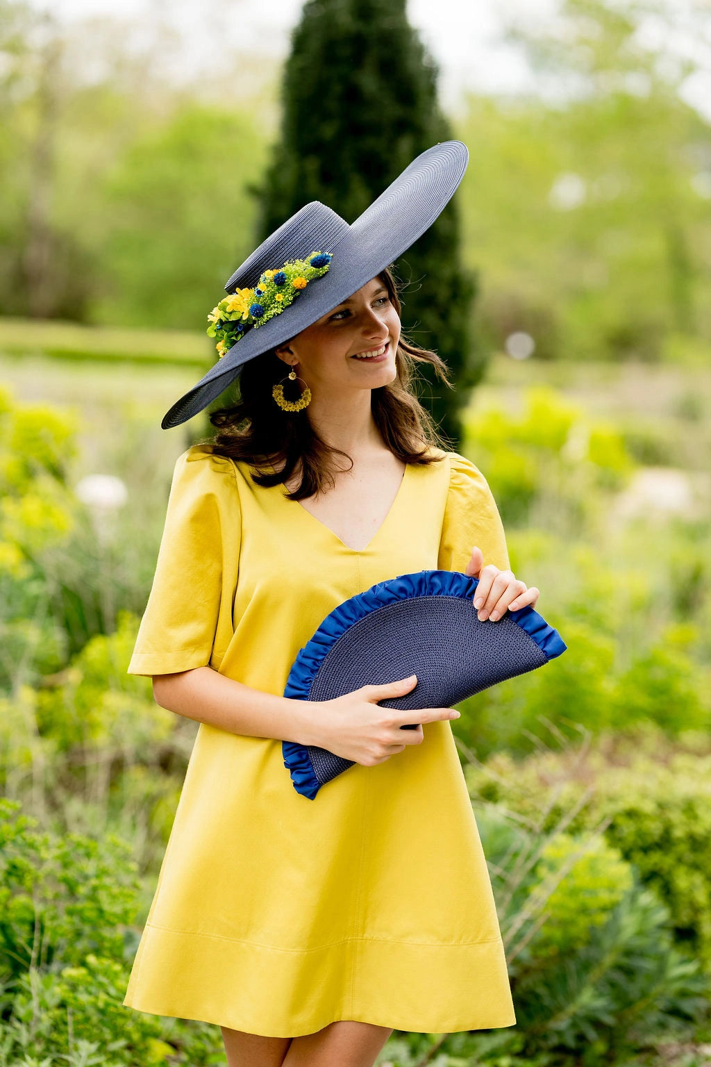 Jeune femme habillée de jaune tenant à la main une pochette en demie lune avec des fronces qui dépassent comme un éventail de couleur bleue. Créé par Bellemond.