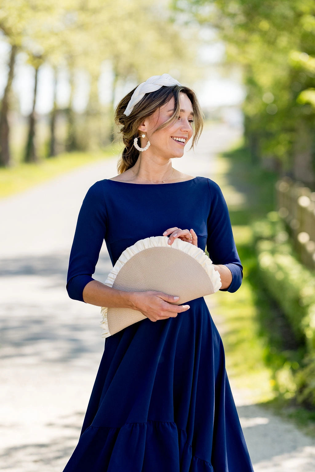 Jeune femme habillée de bleu marine portant une pochette beige en demie lune à volants crème. Créé par Bellemond.